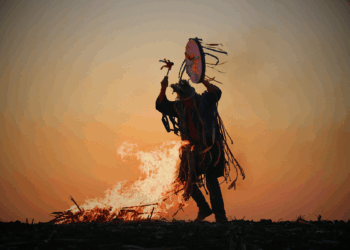 Un chamane danse en jouant du tambour, près d'un feu