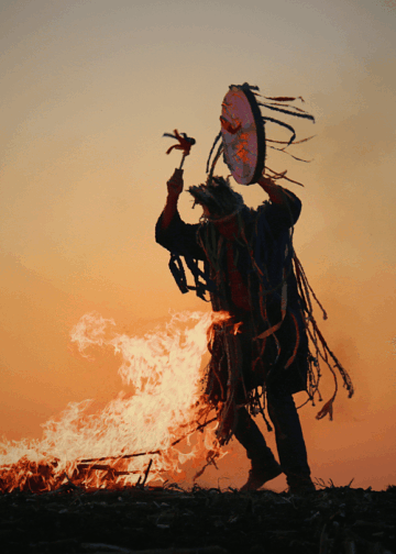 Un chamane danse en jouant du tambour, près d'un feu